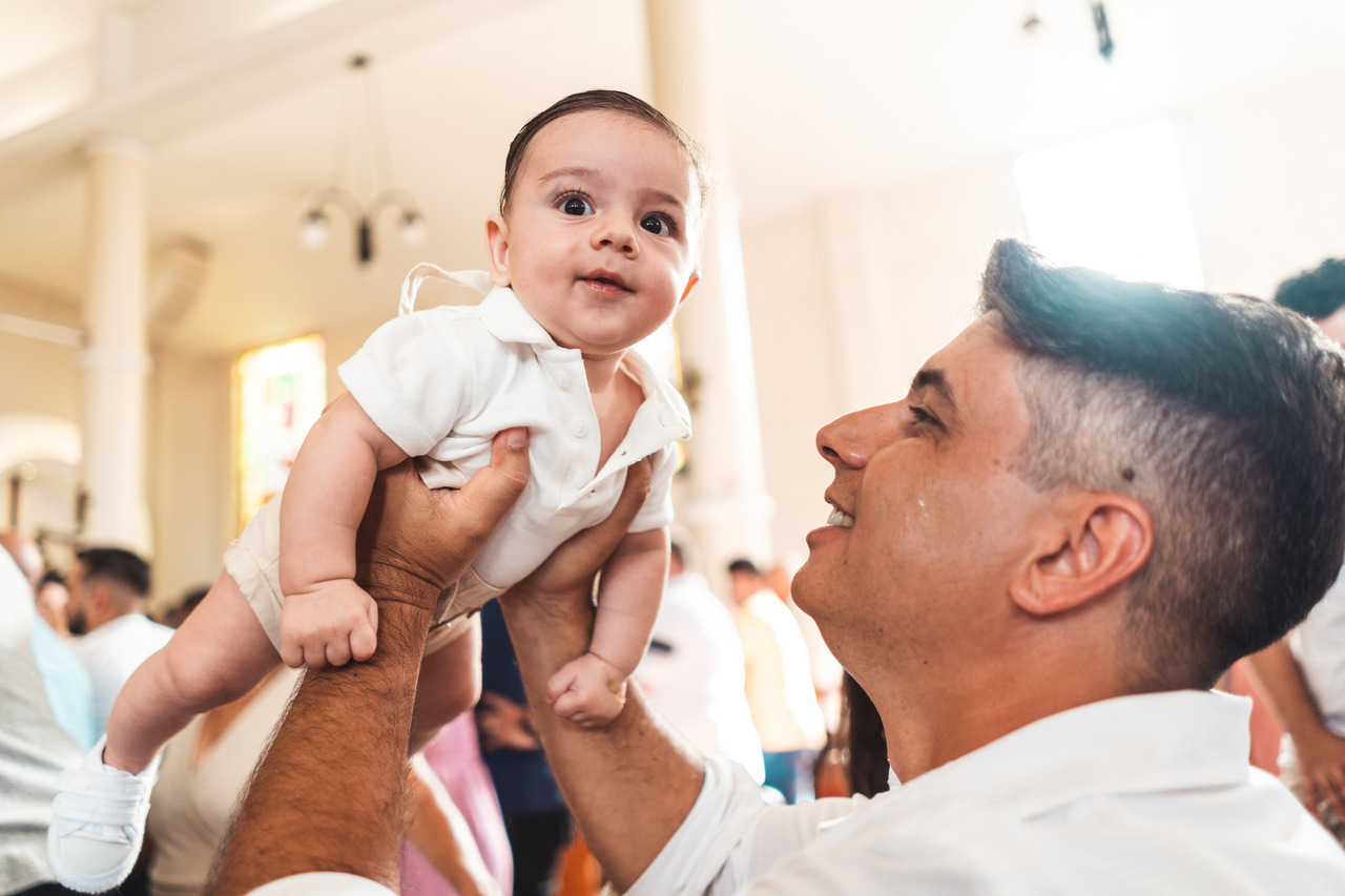 Pai e bebê trocam olhares durante o batizado